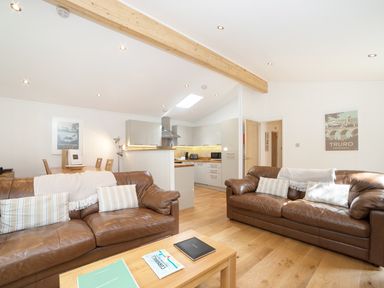 An open living room with two brown leather sofas and an adjoining kitchen at 7 Streamside in Lanreath
