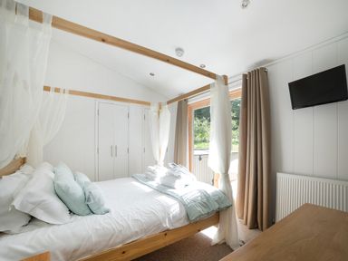 A bedroom with a wooden four-poster bed soft pillows a wardrobe a wall-mounted television and curtains at 7 Streamside in Lanreath