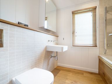 A bathroom with a wall-mounted sink toilet window with blinds and a bathtub at 7 Streamside in Lanreath