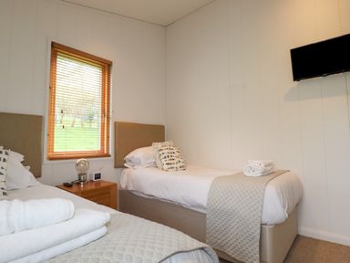 A bedroom with two single beds a wooden window and a wall mounted television at 7 Streamside Lanreath