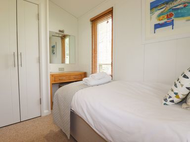 A bedroom with a bed with folded towels on top a desk with a mirror a window with wooden blinds and a closet at 7 Streamside Lanreath