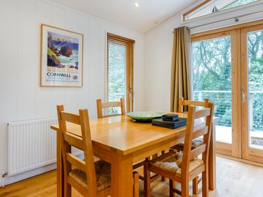 A dining area with a wooden table and four chairs near windows and glass doors at 8 Streamside in Lanreath