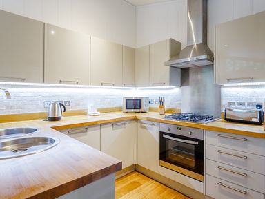 A kitchen with wooden countertops a stainless steel sink a kettle a microwave a gas stove an oven knives and a toaster at 8 Streamside Lanreath