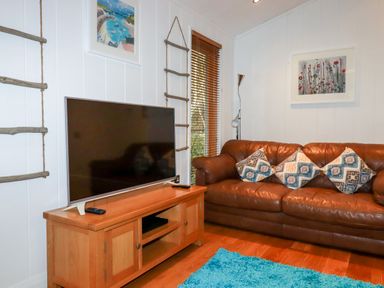 A brown leather sofa with patterned cushions near a wooden TV stand with a television in a living room at 2 Stonerush Valley Lanreath