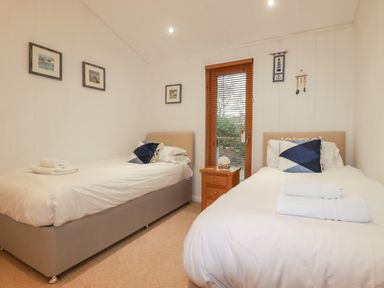 A bedroom with two single beds a wooden nightstand and door with blinds at 2 Stonerush Valley in Lanreath