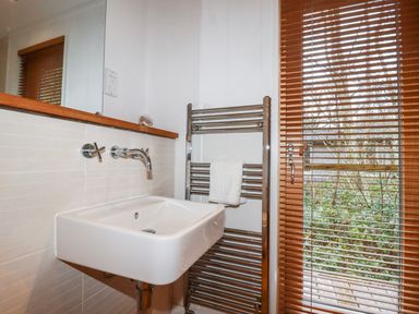 A bathroom with a wall-mounted sink a heated towel rail with a towel and wooden blinds on a window at 2 Stonerush Valley in Lanreath