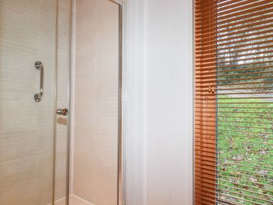 A shower enclosure with glass door next to a window with wooden blinds at 2 Stonerush Valley Lanreath