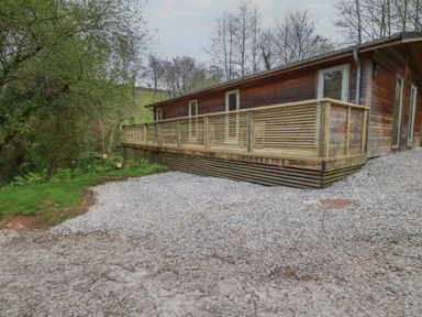 A wooden house with a deck and gravel driveway surrounded by trees at 2 Stonerush Valley in Lanreath