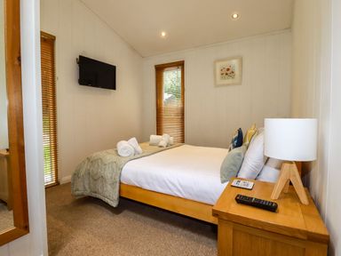 A bedroom with a double bed a wooden nightstand with a lamp and TV on the wall at 2 Stonerush Valley in Lanreath