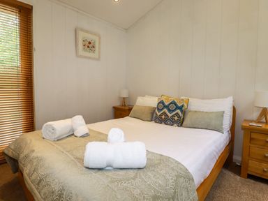 A bedroom with a bed with pillows and rolled towels and bedside tables with lamps at 2 Stonerush Valley in Lanreath