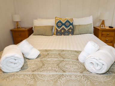 A bed with pillows and rolled towels on a patterned bedspread with bedside tables and lamps at 2 Stonerush Valley in Lanreath