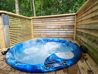An outdoor hot tub with blue patterned edges on a wooden deck surrounded by wooden fencing at 2 Stonerush Valley in Lanreath