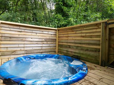 An outdoor hot tub with blue and white swirls surrounded by wooden fencing and trees at 2 Stonerush Valley in Lanreath