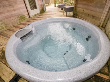 An outdoor hot tub on a wooden deck with two wicker chairs and a table at 9 Stonerush Valley in Lanreath