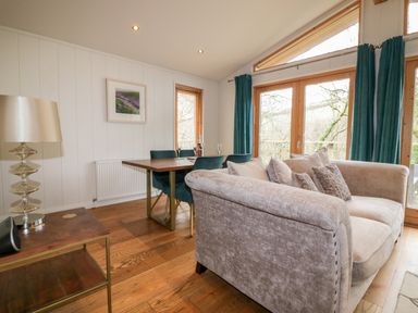 A living area with a beige sofa blue dining chairs wooden table lamp and large windows with blue curtains at 9 Stonerush Valley in Lanreath
