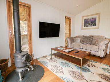 A living room with a wood stove a wall-mounted TV a sofa and a coffee table at 9 Stonerush Valley in Lanreath
