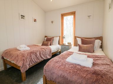 A bedroom with two single beds with pink blankets and pillows a window with blinds a bedside table with a lamp and clock at 9 Stonerush Valley Lanreath