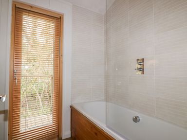 A bathroom with a bathtub and wooden blinds on a door at 9 Stonerush Valley in Lanreath