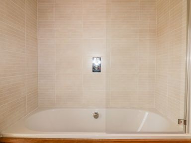 A bathtub with beige tiled walls and a glass shower screen at 9 Stonerush Valley in Lanreath