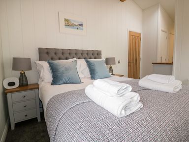 A bedroom with a double bed two pillows on the bed bedside tables with lamps and a wooden door at 9 Stonerush Valley in Lanreath