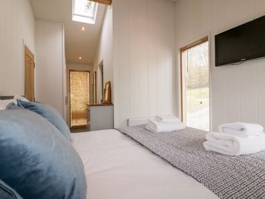 A bedroom with a bed with folded towels on it a window with blinds a wall-mounted TV a dresser with a mirror and a skylight at 9 Stonerush Valley in Lanreath
