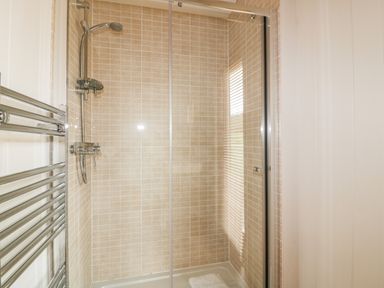 A shower area with beige tiled walls glass door and a wall-mounted showerhead at 9 Stonerush Valley in Lanreath