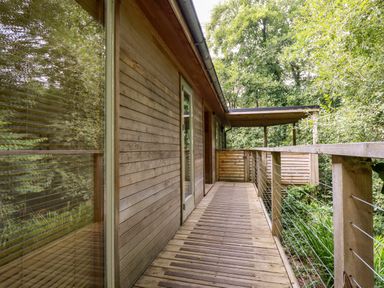 A wooden deck with railing and a door surrounded by trees at 9 Stonerush Valley in Lanreath