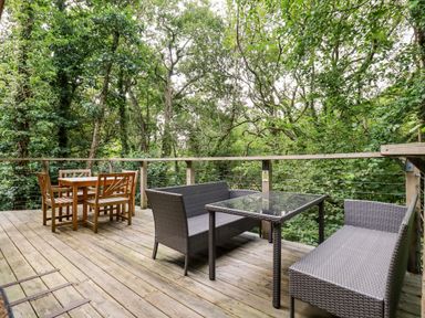 An outdoor wooden deck with two seating areas surrounded by trees at 9 Stonerush Valley in Lanreath