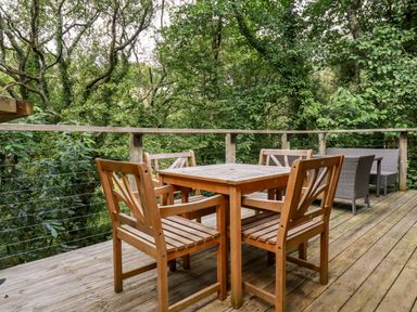 A wooden deck with a wooden table and four chairs surrounded by trees at 9 Stonerush Valley in Lanreath