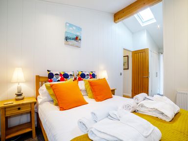 A bedroom with a bed with orange and patterned pillows bedside tables with lamps and folded white towels on the bed at 2 Water's Edge in Lanreath