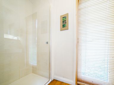 A bathroom shower area with glass door next to a wall with picture frame and a window with blinds at 2 Water's Edge Lanreath