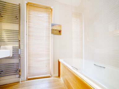 A bathroom with a bathtub wooden panel blinds on window and a chrome towel radiator at 2 Waters Edge in Lanreath