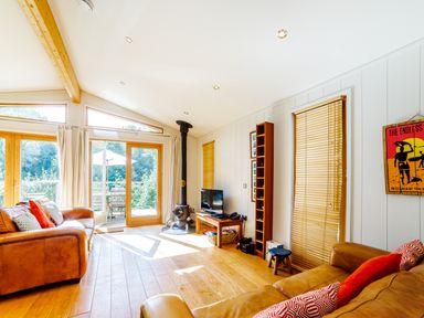 A living room with leather sofas wooden floor wood stove and a television at 2 Water's Edge in Lanreath