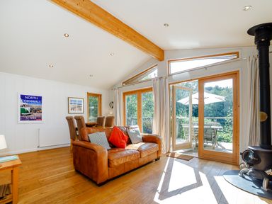 A living room with a leather sofa and wooden dining table next to large glass doors opening to a patio at 2 Water's Edge Lanreath
