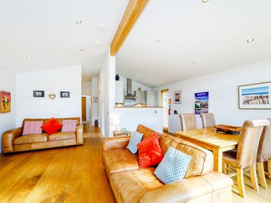 A living room with two leather sofas and cushions a wooden dining table with four chairs and a kitchen area at 2 Water's Edge in Lanreath