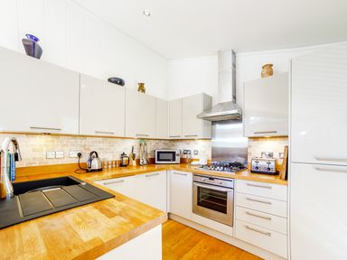 A kitchen with wooden countertops and white cabinets including a microwave kettle toaster oven and sink at 2 Water's Edge in Lanreath