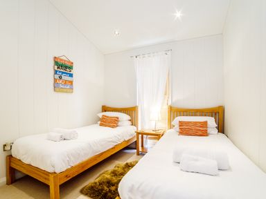 A bedroom with two single wooden beds white bedding and orange pillows at 2 Water's Edge in Lanreath