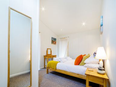 A bedroom with a wooden bed orange and yellow pillows bedside table with lamp and a mirror leaning against the wall at 2 Water's Edge in Lanreath