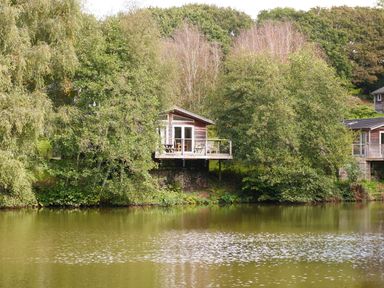 A house by a lake surrounded by trees at 2 Water's Edge in Lanreath