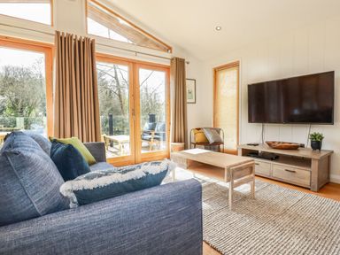 A living room with a blue sofa pillows wooden coffee table wall mounted TV and large windows at 4 Water's Edge in Lanreath