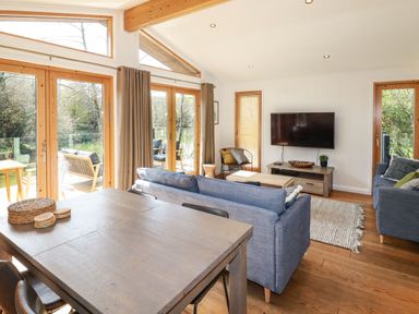 A living room with blue sofas a wooden dining table and large glass doors opening to a balcony at 4 Water's Edge in Lanreath