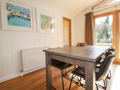 A dining area with a wooden table and black chairs next to glass doors and framed artwork on the wall at 4 Water's Edge in Lanreath