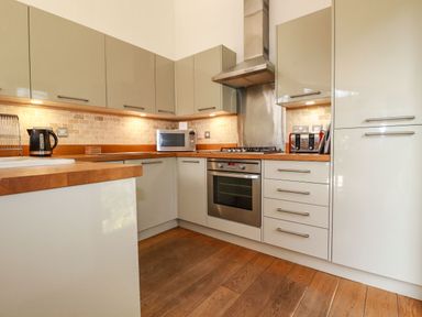 A kitchen with wooden countertops, cabinets, stainless steel oven, microwave, kettle, and toaster at 4 Water's Edge in Lanreath