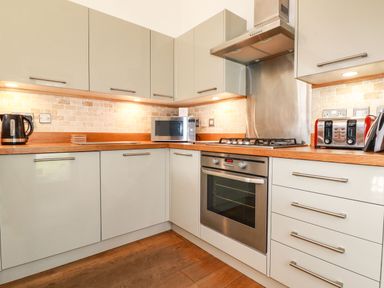 A kitchen with white cabinets wooden countertops an oven a stove microwave toaster and kettle at 4 Water's Edge Lanreath