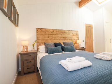 A bedroom with a bed with blue bedding two bedside tables with lamps and flowers at 4 Water's Edge in Lanreath