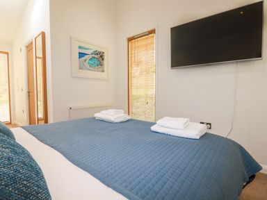 A bedroom with a blue bedspread a wall-mounted TV and a window with wooden blinds at 4 Water's Edge in Lanreath
