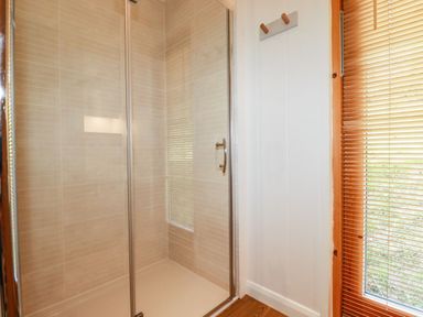 A shower with glass doors next to a window with blinds at 4 Water's Edge in Lanreath