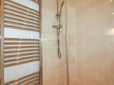A shower area with a wall-mounted showerhead and a metal towel radiator at 4 Water's Edge in Lanreath