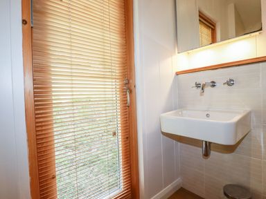 A bathroom with a wall-mounted sink next to a door with wooden blinds at 4 Water's Edge in Lanreath