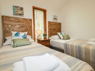 A bedroom with two single beds wooden headboards a nightstand with a lamp and window blinds at 4 Waters Edge in Lanreath